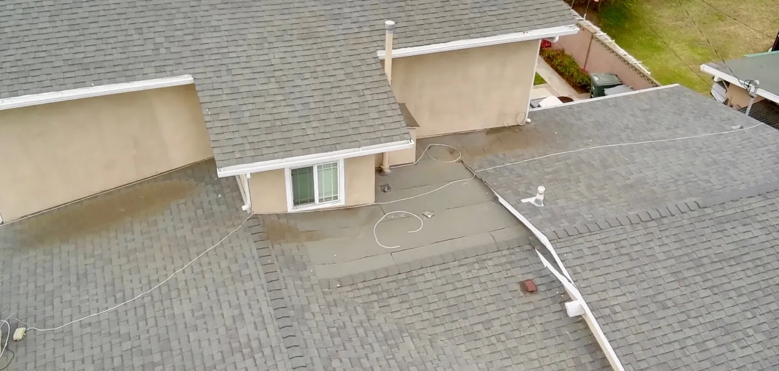 Aerial view of a worn shingle roof with a stained flat section before replacement