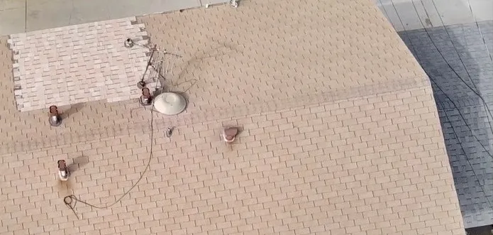 Aerial view of a faded tan shingle roof with patched sections before replacement
