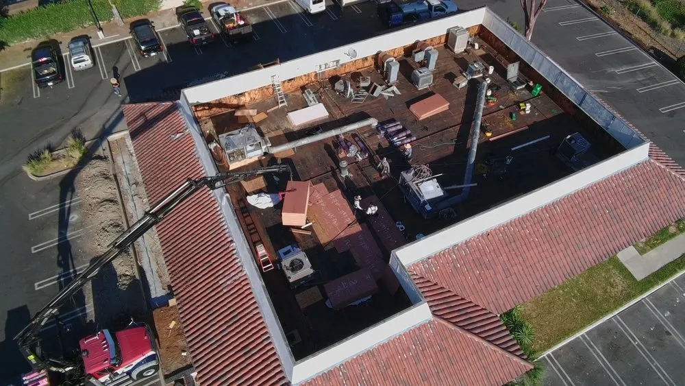 Aerial view of a commercial roof during tear-off with a boom truck and crew