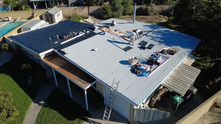 Aerial view of a flat-roof home beside a pool during tear-off