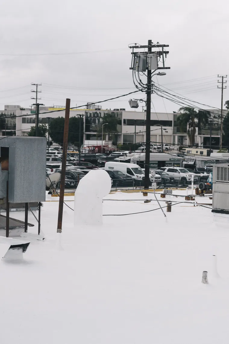 White-coated flat roof with vent penetrations beneath an overcast sky