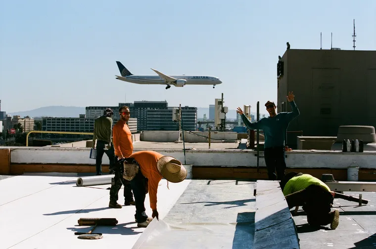 Swell Roofing crew on a commercial flat roof as a jet lands nearby