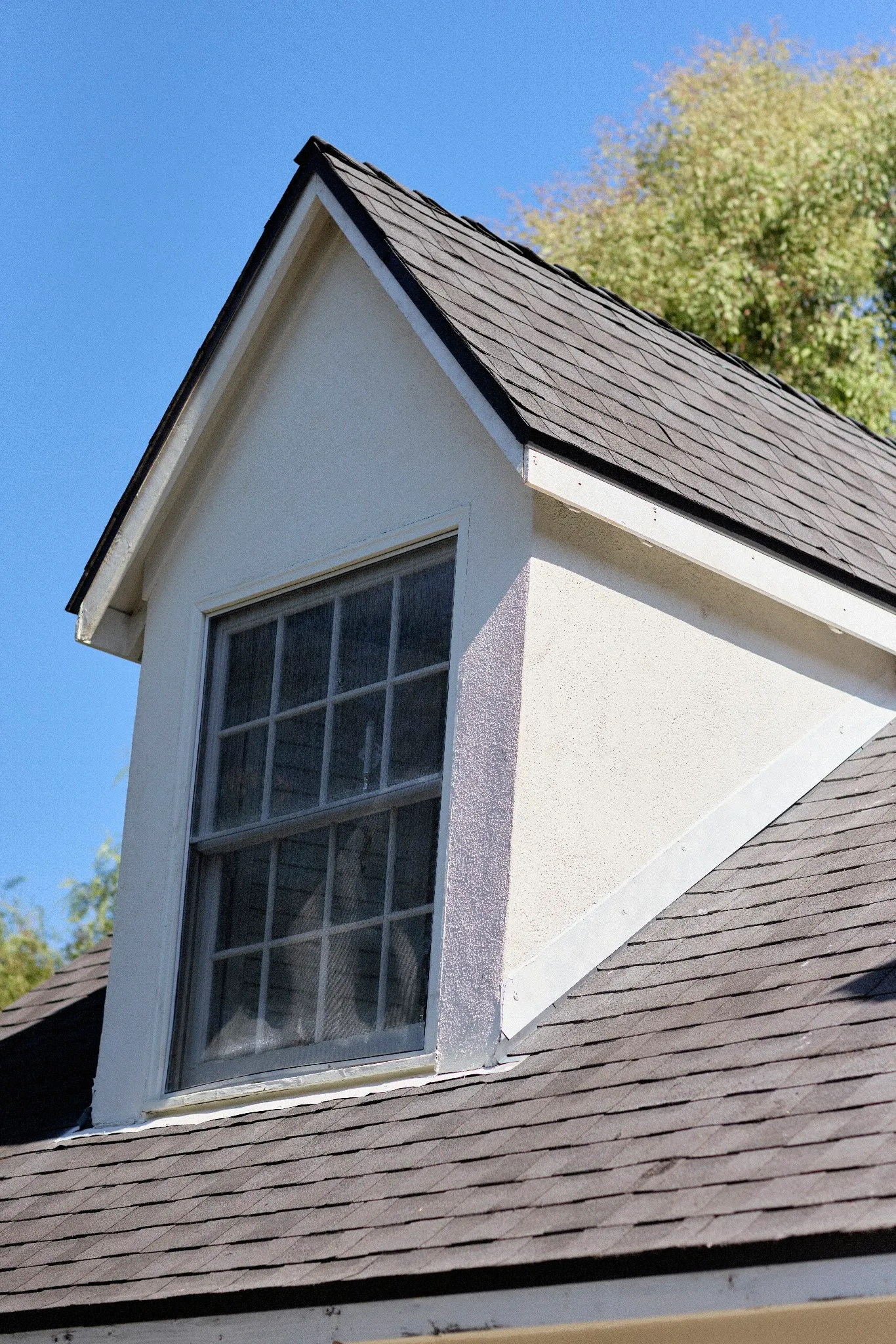 Finished charcoal architectural shingles around a white gable dormer