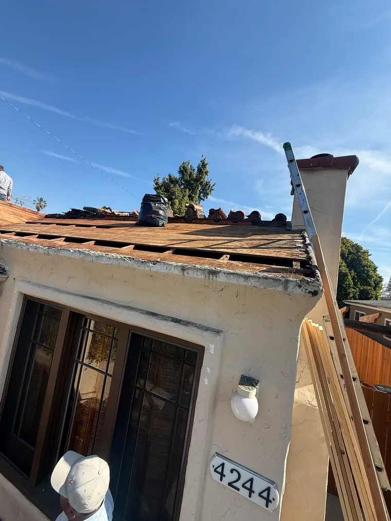 Spanish-style house mid tear-off with an extension ladder and tiles stacked at the ridge