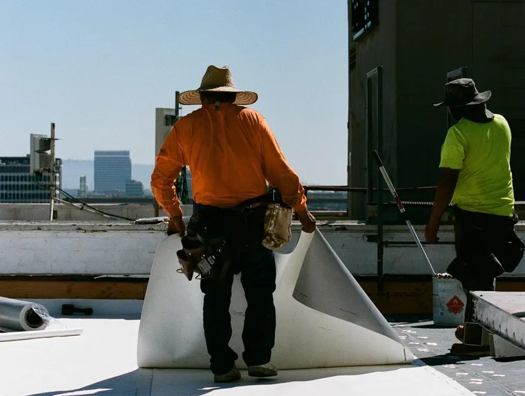 Crew rolling membrane beside a commercial roof parapet