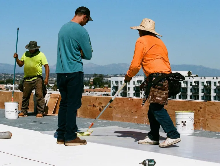 Three workers rolling adhesive across a commercial roof field