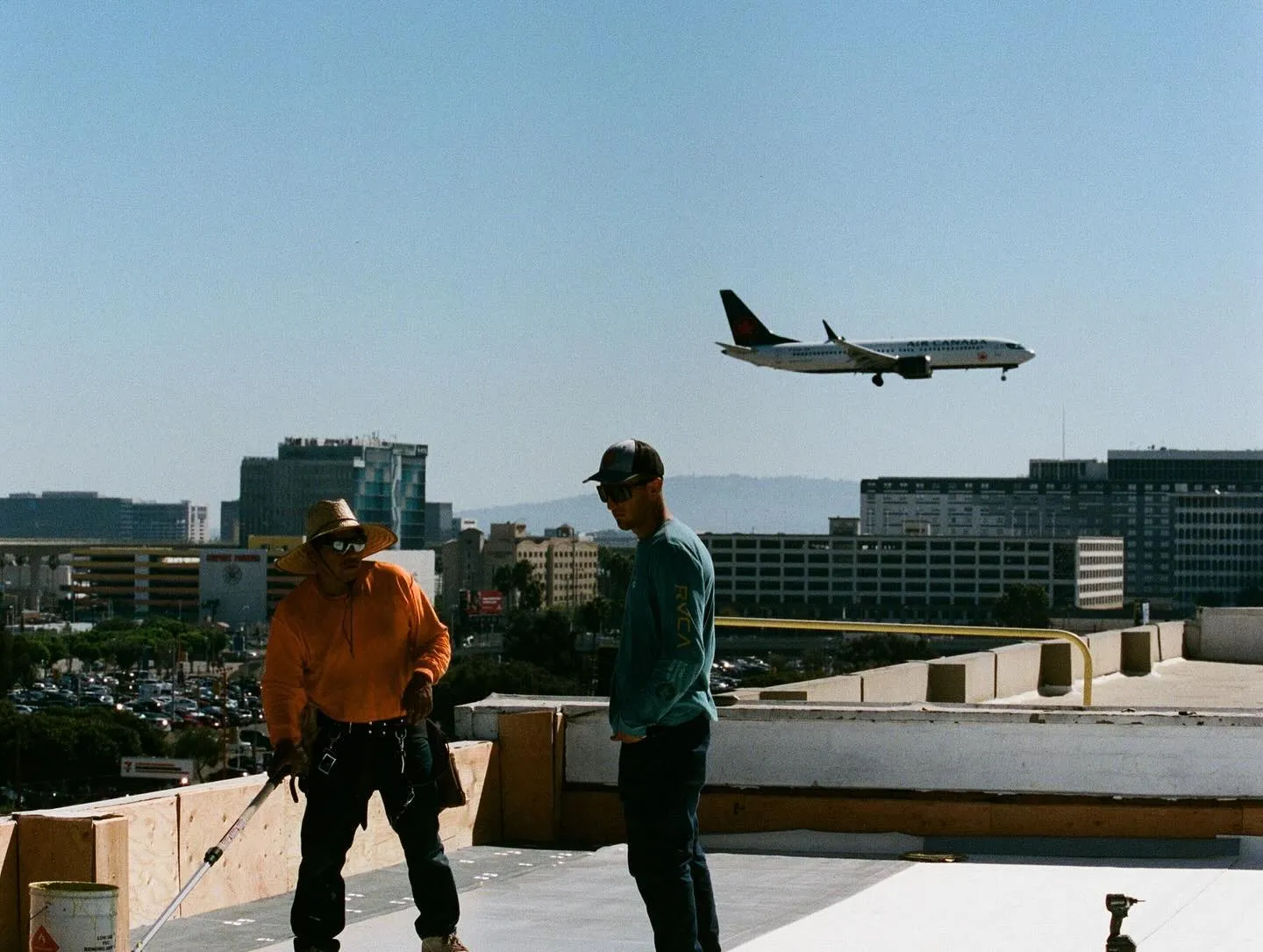 Two roofers working on a flat roof as a jet passes overhead