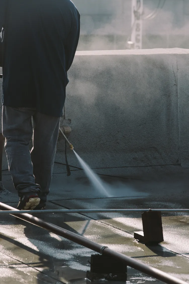 Close view of pressure-washing spray lifting buildup from a flat roof