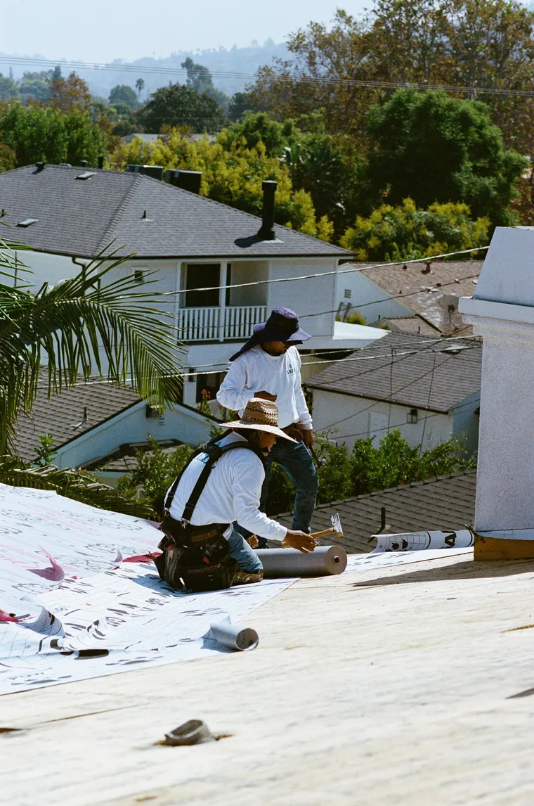 Roofer rolling underlayment across a clean plywood roof deck