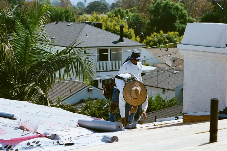 Roofer unrolling synthetic underlayment across a residential roof