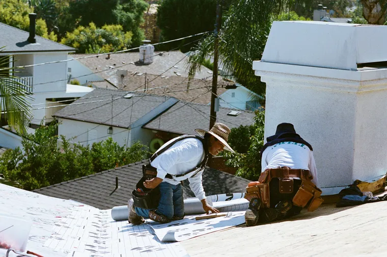 Roofers working with underlayment beside a masonry chimney