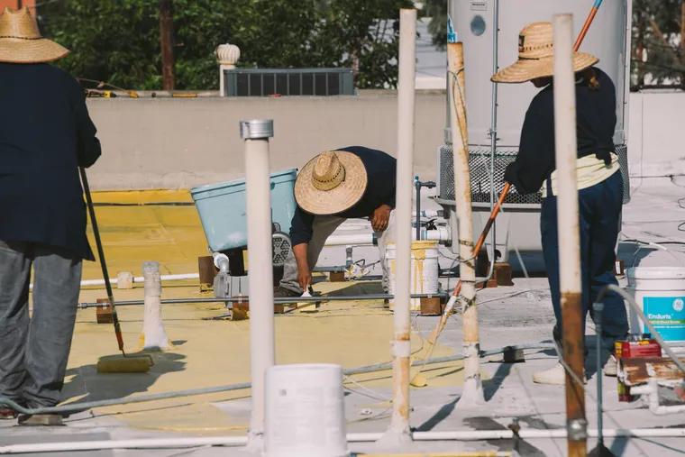 Three workers coating a flat roof around vent pipes