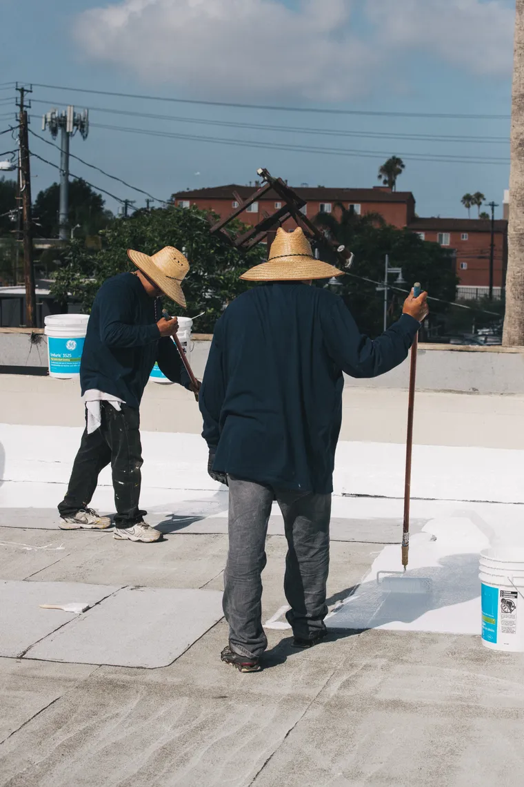 Two workers rolling white coating across a flat roof