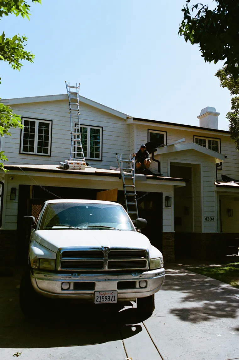 White house with ladders and a work truck staged for roofing