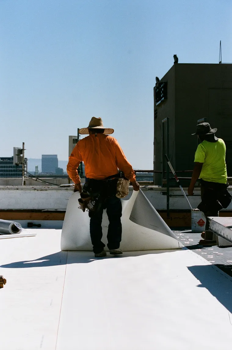 Worker moving a white membrane roll across a commercial roof