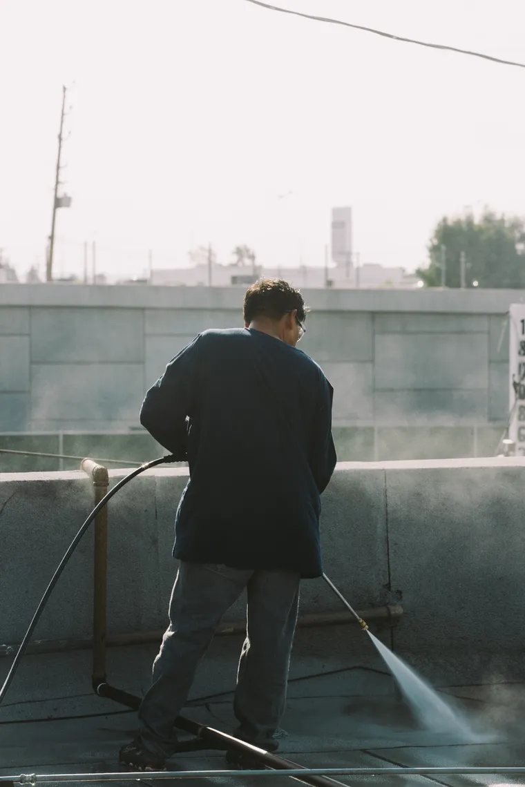 Worker pressure washing a section of commercial flat roof
