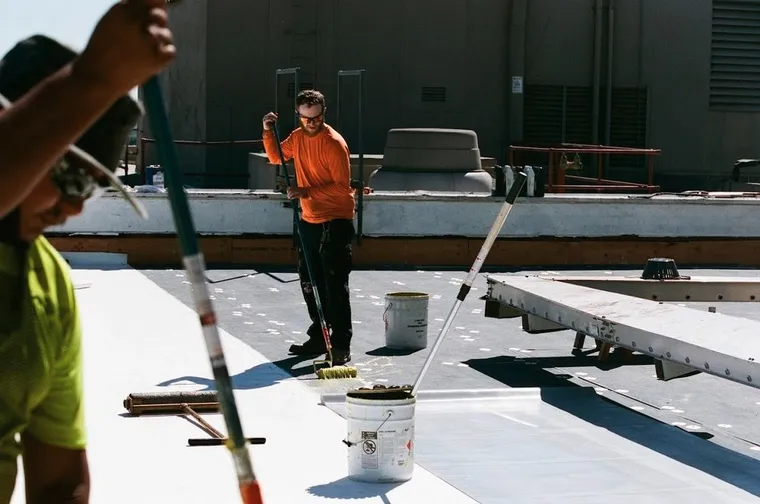 Worker rolling coating across a white commercial flat roof