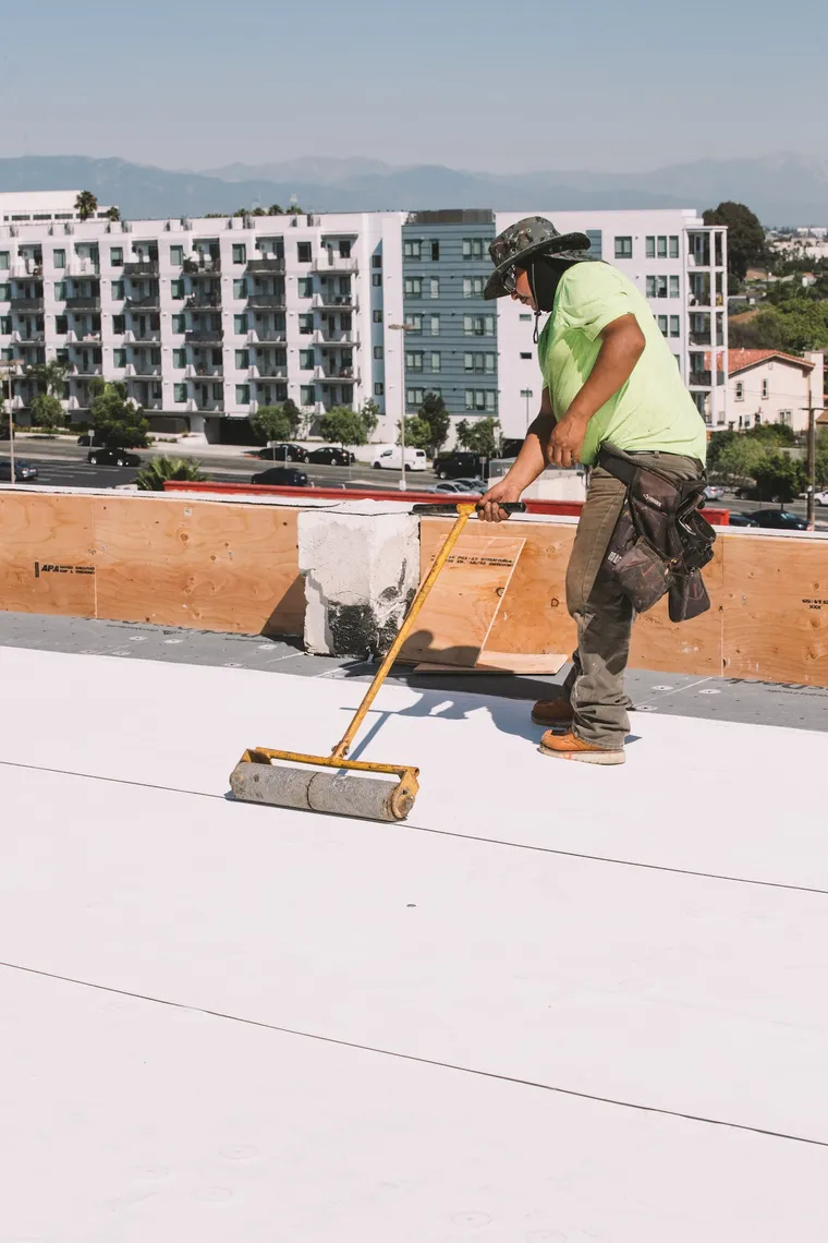 Worker rolling yellow bonding adhesive across a commercial roof